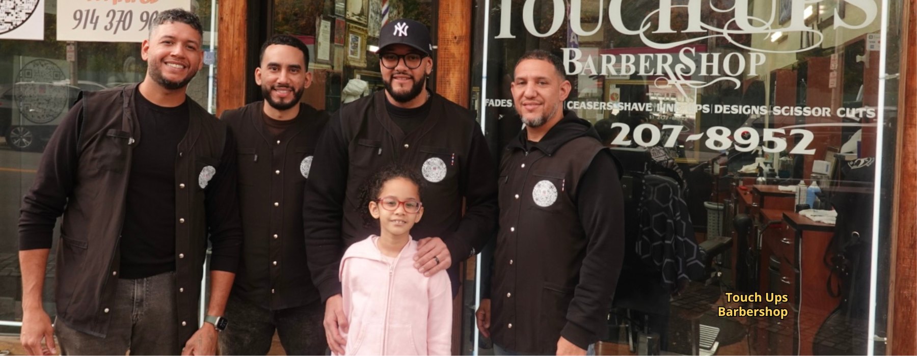 The team and family of Touch Ups Barbershop standing in front of their storefront on South Broadway